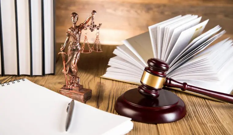 A wooden table with a statue of justice and books.